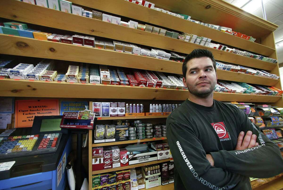 Brian Vincent poses in front of a large display of tobacco products at Vincent’s Country Store in Westminster, Mass., Thursday, Nov. 6, 2014.