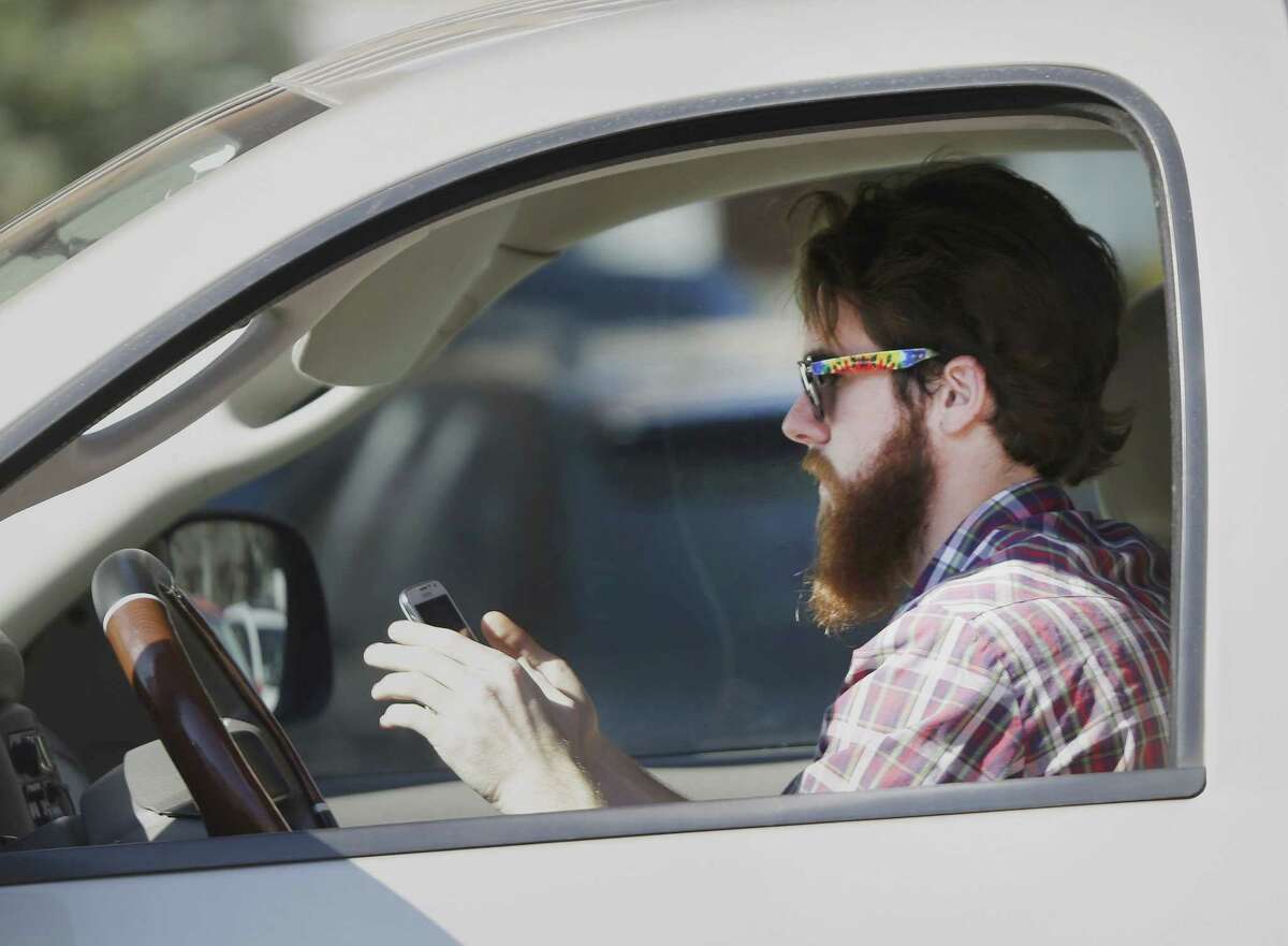 In this file photo, a man uses his cell phone as he drives through traffic. In a 2013 survey, 98 percent of motorists who own cellphones and text regularly were aware of the dangers, yet three-quarters of them admit to texting while driving, despite laws against it in some states.