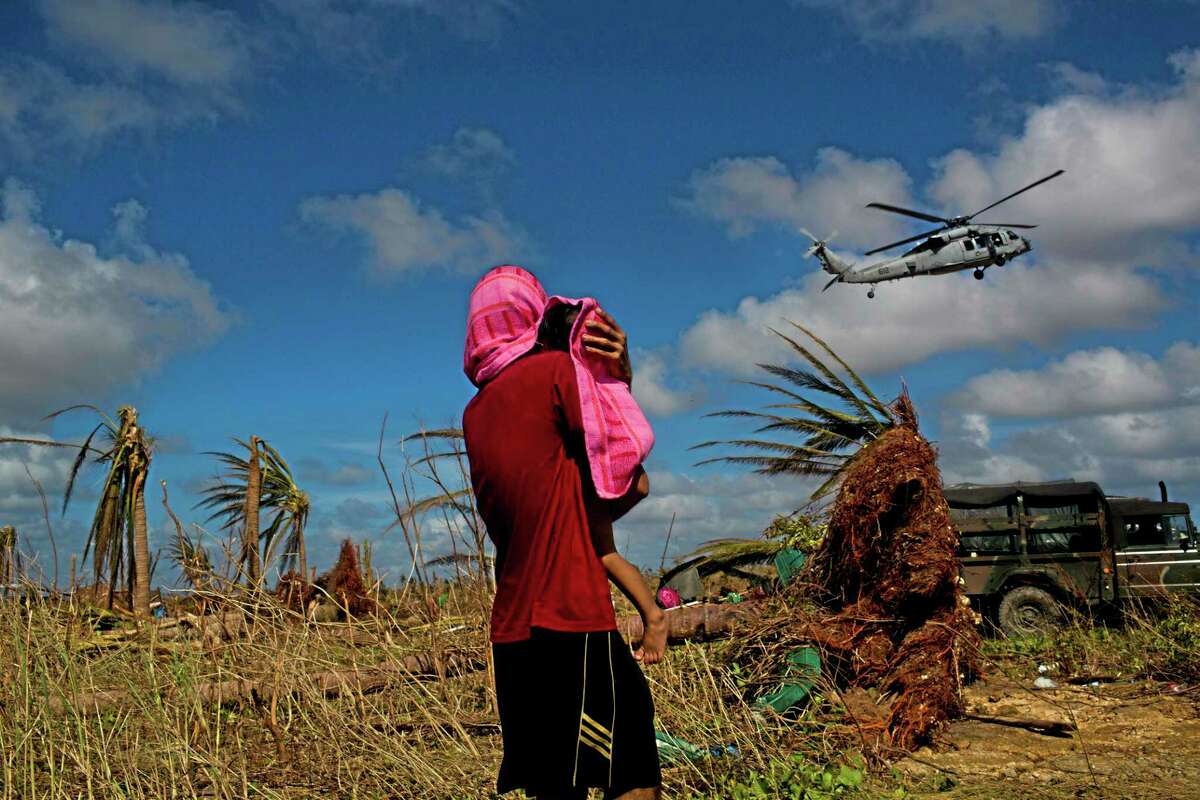 A Typhoon Haiyan survivor carries a child wrapped in a towel as he watches a helicopter landing to bring aid to the destroyed town of Guiuan, Samar Island, Philippines, Friday.