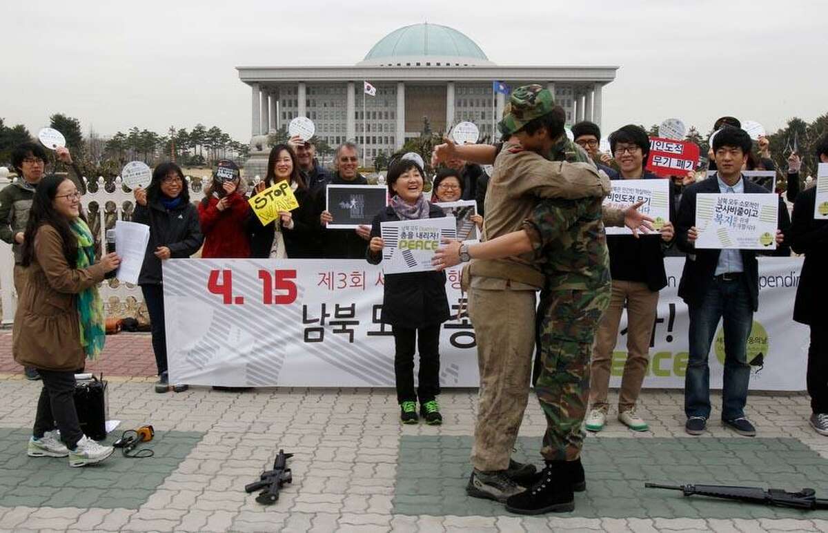 Anti-war activists wearing military clothes of a North, left, and South Korea hug each other during a rally to mark Global Day of Action on Military Spending in front of the National Assembly in Seoul, South Korea, Monday, April 15, 2013. They demanded peaceful unification of the Korean peninsula. Elsewhere in the region, however, the focus remained on the threat of a missile launch by the North as U.S. Secretary of State John Kerry wrapped up a tour to coordinate Washington's response with Beijing, North Korea's most important ally, as well as Seoul and Tokyo. (AP Photo/Ahn Young-joon)