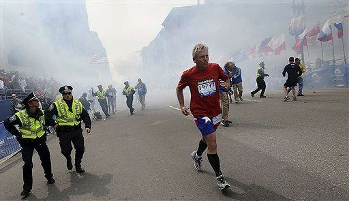 A Boston Marathon competitor and Boston police run from the area of an explosion near the finish line in Boston, Monday, April 15, 2013. (AP Photo/MetroWest Daily News, Ken McGagh) MANDATORY CREDIT