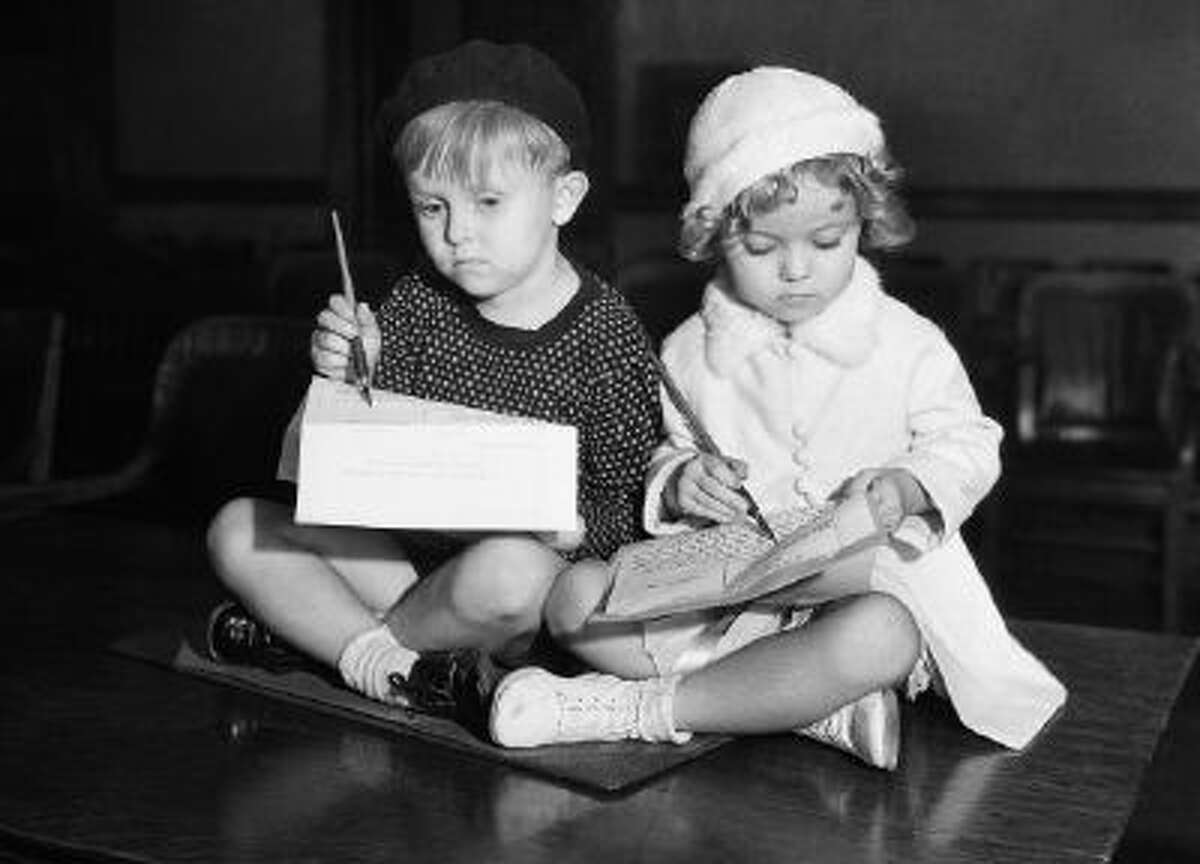 Flaming youth will be depicted on the screen in the from of these two tots, whose respective parents have signed contracts for them to appear in a series of baby shorts on October 10, 1932. They are Georgie Smith and Shirley Temple, and photo shows 'em signing on the dotted line, just as their parents did - at least they're scratching with gusto.