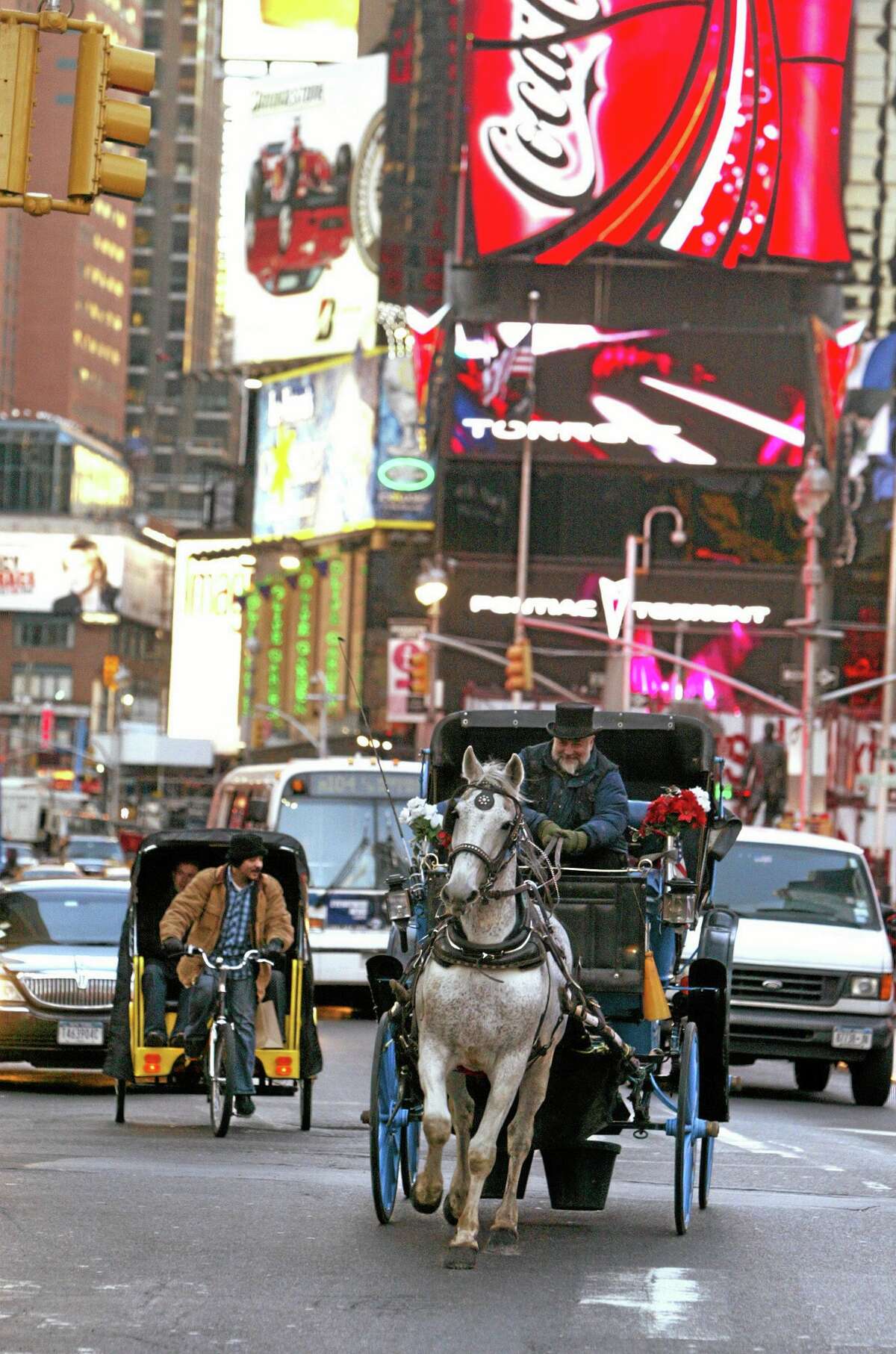 FILE- In this March 1, 2006, file photo, a pedicab driver, left, and a horse-drawn carriage make their way down Broadway in New York's Times Square. New York City Mayor Bill de Blasio seeks to shut down the cityís horse-drawn-carriage industry, believing that it was less than humane to put horses on busy New York City streets. Carriage-horse drivers counter that their industry provides homes for surplus horses from farms and the racing industry that would otherwise be shipped off to slaughterhouses. (AP Photo/Mary Altaffer, File)