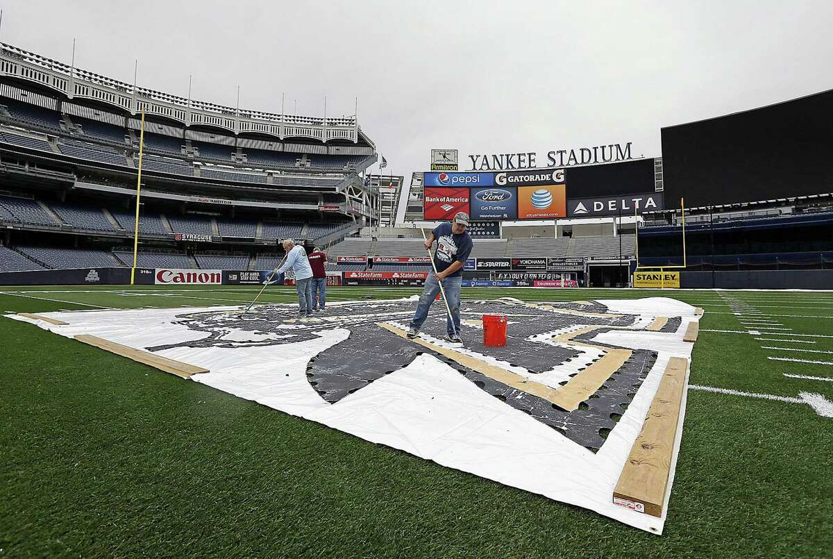 Grounds crew workers paint the Army Black Knights logo on the turf at midfield on Wednesday at Yankee Stadium in New York.