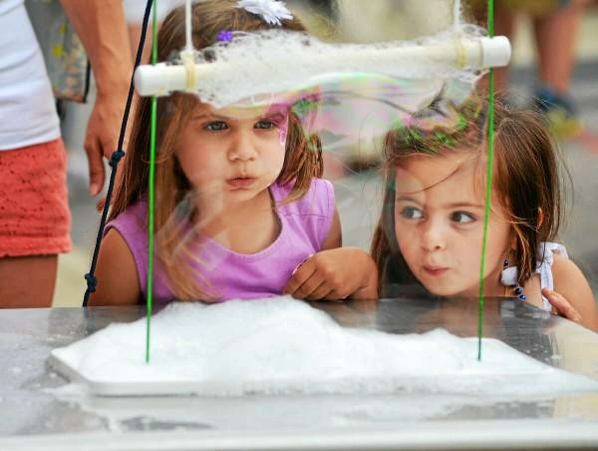 Tessa Paganini, left, of Torrington, and Piper Relihan or Litchfield, both 3, play with the bubble station set up in front of KidsPlay children's museum during Main Street Marketplace in Torrington. John Berry - Register Citizen.