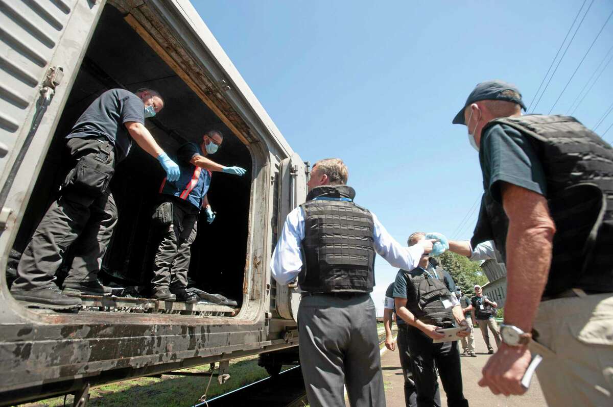 Deputy head of the OSCE mission to Ukraine Alexander Hug, center back to the camera, speaks to a member of Netherlands’ National Forensic Investigations Team on the platform as a refrigerated train loaded with bodies of the passengers departs the station in Torez, eastern Ukraine, 15 kilometers (9 miles) from the crash site of Malaysia Airlines Flight 17, Monday, July 21, 2014. (AP Photo/Evgeniy Maloletka)