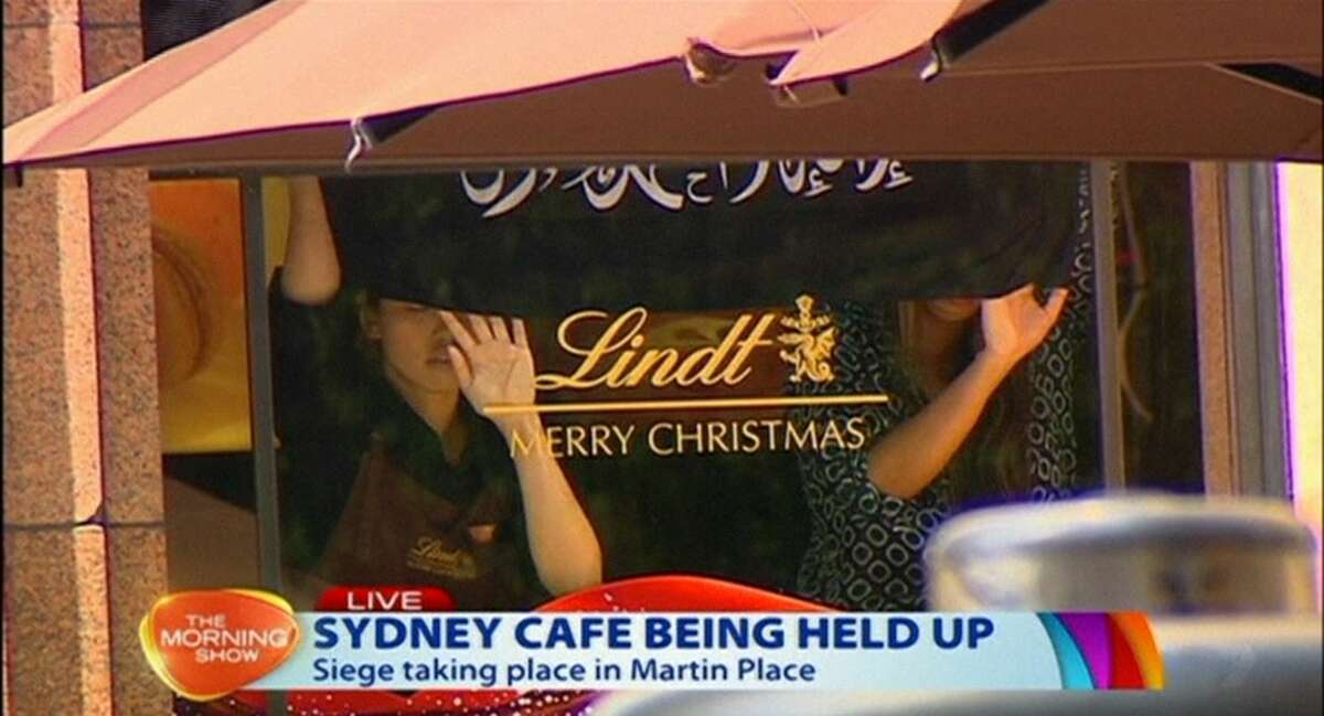 This image taken from video shows people holding up what appeared to be a black flag with white Arabic writing on it, inside a cafe in Sydney, Australia Monday, Dec. 15, 2014. An apparent hostage situation was unfolding inside the chocolate shop and cafe in Australia’s largest city on Monday, where several people could be seen through a window with their hands held in the air.