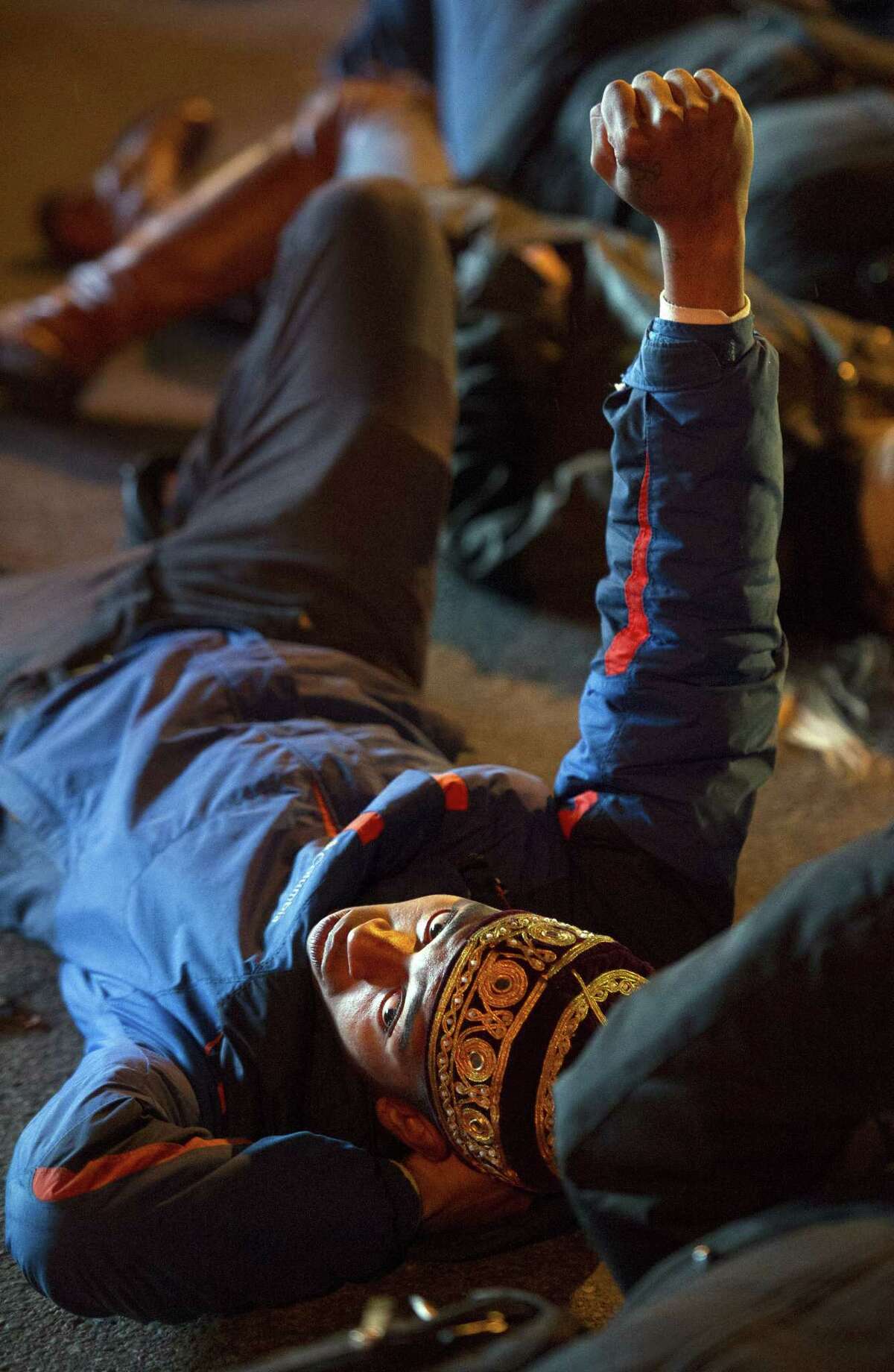 Deon Johnson, 19, of Washington, DC, raises his fist as he and others take part in a four and-a-half minute "die-in" while blocking an intersection in downtown,Washington, Friday, Dec. 5, 2014, during a demonstration against the deaths of two unarmed black men at the hands of white police officers in New York City and Ferguson, Mo. (AP Photo/Cliff Owen)