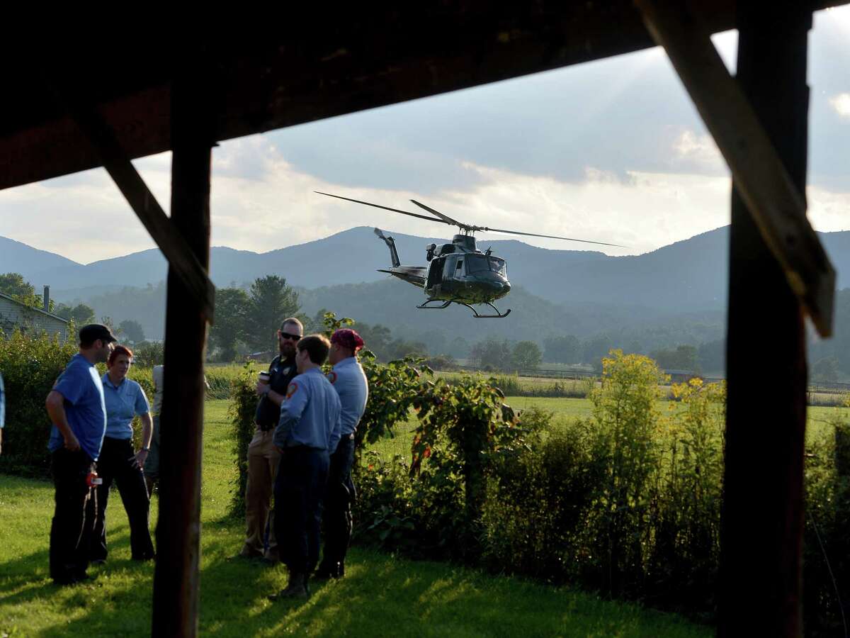 A helicopter takes off near search team members who wait for their turn to join the search for a missing pilot at the mobile command center in Deerfield, Va., on Wednesday, Aug. 27, 2014.
