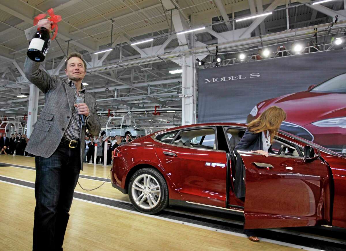 FILE - In this June 22, 2012 file photo, Tesla Motors Inc. CEO Elon Musk holds up a bottle of wine given as a gift from one of their first customers, right, during a rally at the Tesla factory in Fremont, Calif. When billionaire entrepreneur Elon Musk published fanciful plans to shoot capsules full of people at the speed of sound through a tube connecting Los Angeles and San Francisco, he asked the public to perfect his rough plans. From tinkerers to engineers, the race is on. (AP Photo/Paul Sakuma, File)