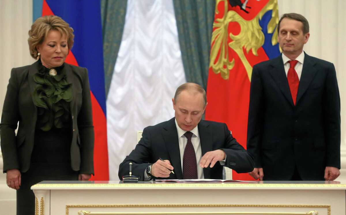 Russian President Vladimir Putin, flanked by Upper House Speaker Valentina Matviyenko, left, and Lower House Speaker Sergei Naryshkin, signs bills making Crimea part of Russia in the Kremlin in Moscow, Friday, March 21, 2014. President Vladimir Putin completed the annexation of Crimea on Friday, signing the peninsula into Russia at nearly the same time his Ukrainian counterpart sealed a deal pulling his country closer into Europe's orbit. (AP Photo/Sergei Chirikov, Pool)