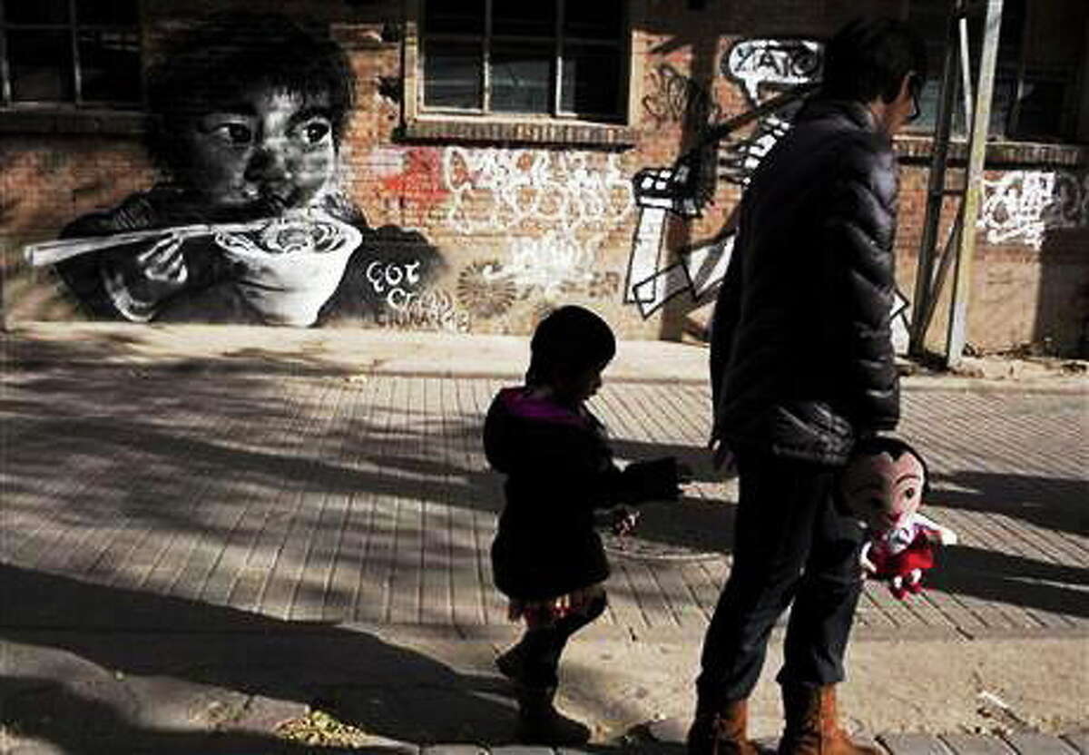 FILE - In this Nov. 17, 2013 file photo, a woman leads a child while holding a doll as they walk near mural depicting a child eating in Beijing. China on Saturday, Dec. 28, 2013, formally allowed couples to have a second child if one parent is an only child, the first major easing of the 3-decade-old restrictive birth policy.(AP Photo/Ng Han Guan, File)