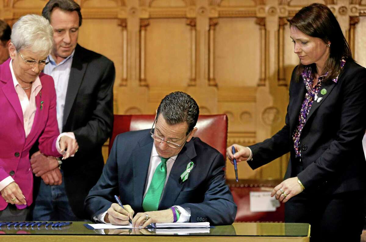 In this April 4, 2013, file photo, Connecticut Gov. Dannel P. Malloy, center, signs legislation at the Capitol in Hartford that includes new restrictions on weapons and large capacity ammunition magazines. Surrounding him are Lt. Gov. Nancy Wyman, left, Neil Heslin, second left, father of shooting victim Jesse Lewis, and Nicole Hockley, right, mother of shooting victim Dylan.