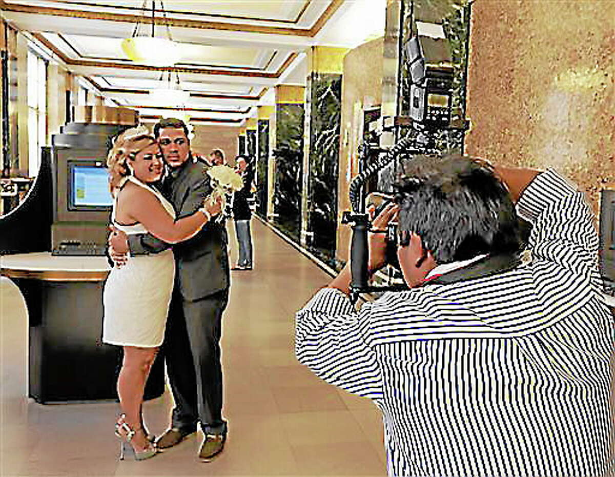 Wedding photographer Braulio Cuenca poses groom Jorge Mejia and bride Irma Aguilar, of the Bronx borough of New York, inside before their ceremony in New York’s Office of the City Clerk, Wednesday Aug. 7, 2013.