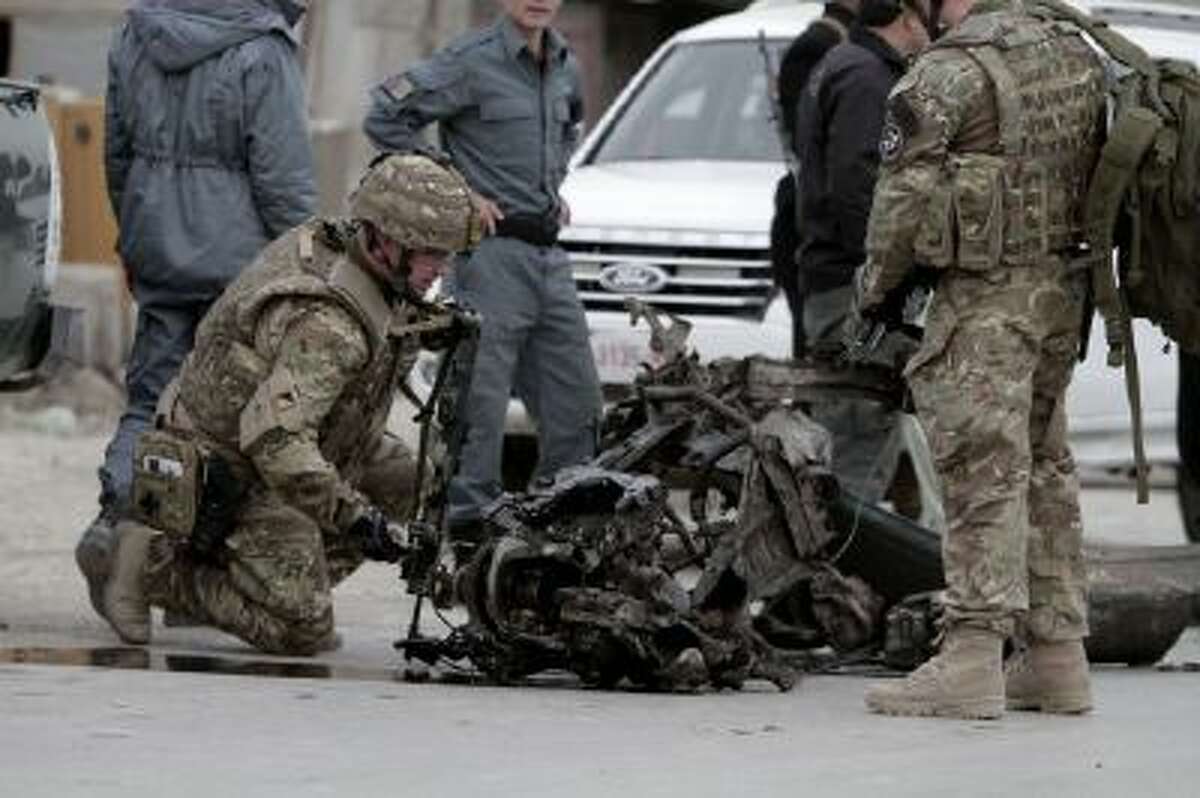 NATO forces examine the remains of a car after a suicide car bomb attack on the Jalalabad-Kabul road in Kabul, Afghanistan, Friday, Dec. 27, 2013.