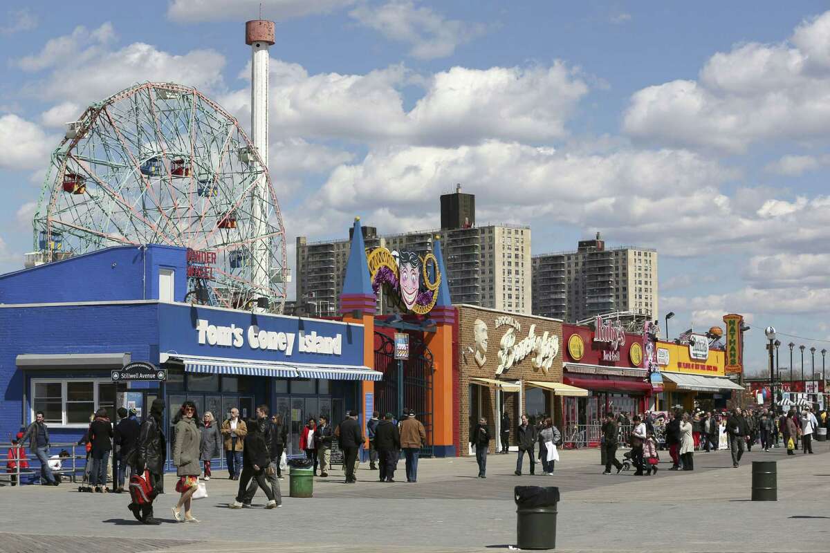 In a 2013 photo, visitors to New York’s Coney Island walk on the boardwalk past the open businesses.