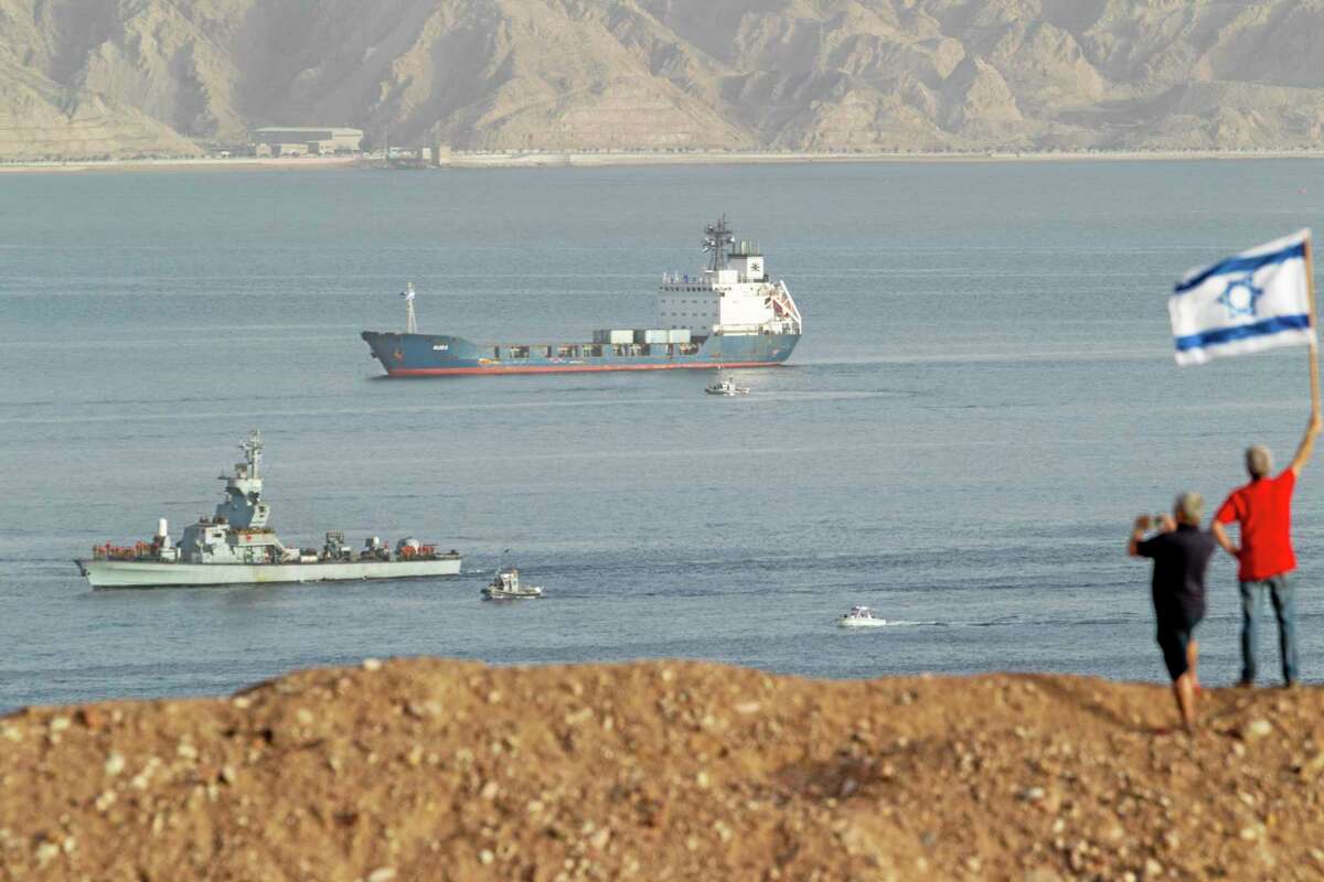 People wave an Israeli flag as the seized Klos-C cargo ship, accompanied by Israeli Naval vessels, approaches the port at the Red Sea resort city of Eilat, southern Israel, Saturday, March 8, 2014. Israeli naval forces raided the ship hundreds of miles from Israel, in the Red Sea on Wednesday and seized dozens of advanced rockets from Iran destined for Palestinian militants in Gaza, according to the Israeli military. The Islamic Jihad, an Iranian-backed militant group in the Gaza Strip, on Friday said it was not involved in a seized missile shipment. (AP Photo/Ariel Schalit)