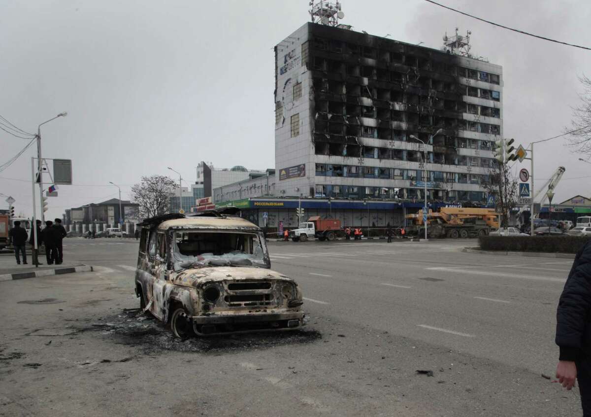 People pass a burned police car outside a burned-out publishing house in central Grozny, Russia, Thursday, Dec. 4, 2014. A gun battle broke out early Thursday in the capital of Russiaís North Caucasus republic of Chechnya, puncturing the patina of stability ensured by years of heavy-handed rule by a Kremlin-appointed leader. The violence erupted hours before Russian President Vladimir Putin began his annual state of the nation address in Moscow.(AP Photo/Musa Sadulayev)