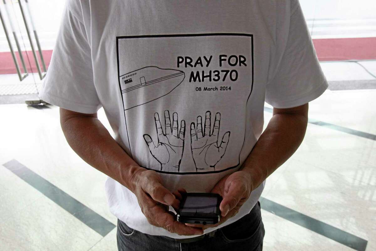A man wearing a T-shirt printing with "Pray for MH370" stands with a smartphone at a hotel in Putrajaya, Malaysia, Saturday, March 15, 2014. The Malaysian jetliner missing for more than a week had its communications deliberately disabled and its last signal came about 7 1/2 hours after takeoff, meaning it could have ended up as far as Kazakhstan or into the southern reaches of the Indian Ocean, Malaysian Prime Minister Najib Razak said Saturday. (AP Photo/Lai Seng Sin)