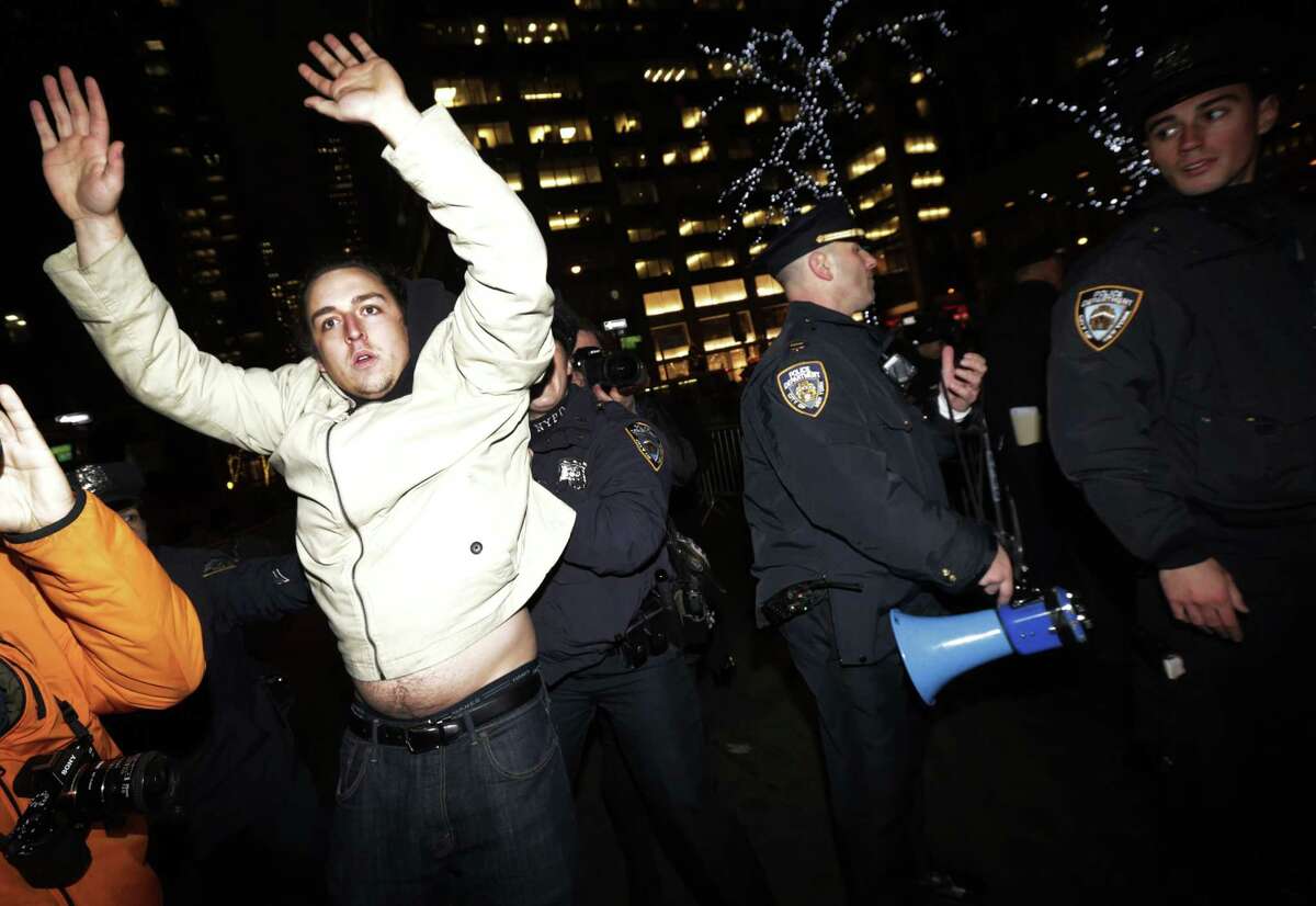 A man, left, holds his hands up as New York City Police officers secure a street near Rockefeller Center during a protest after it was announced that the police officer involved in the death of Eric Garner is not being indicted, Wednesday, Dec. 3, 2014, in New York.