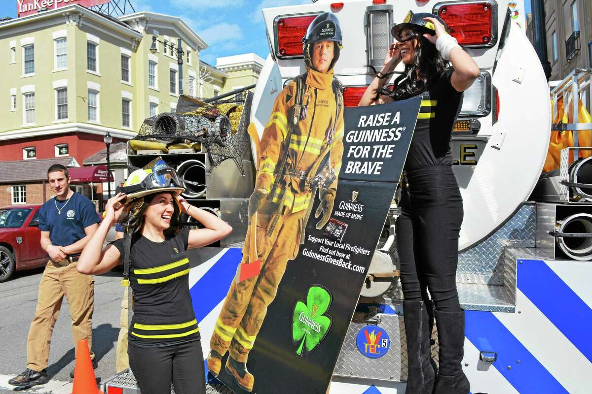 Marguerite Mahon and Monica Larue, who were on hand to support the Guinness Gives Back campaign and the Leary Firefighters Foundation, try on some gear on the back of a Drakeville Volunteer Fire Department tanker truck outside a benefit for the department at Backstage in Torrington Saturday.