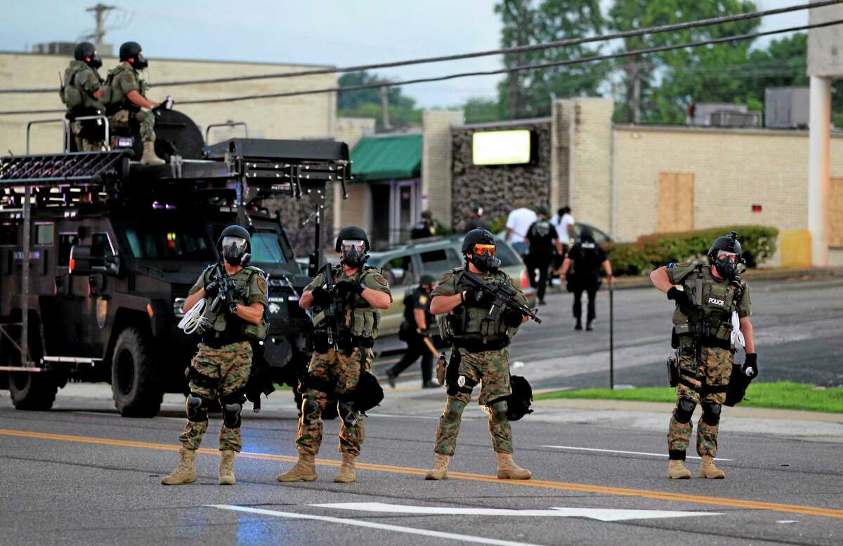 Police wearing riot gear try to disperse a crowd Monday, Aug. 11, 2014, in Ferguson, Mo.