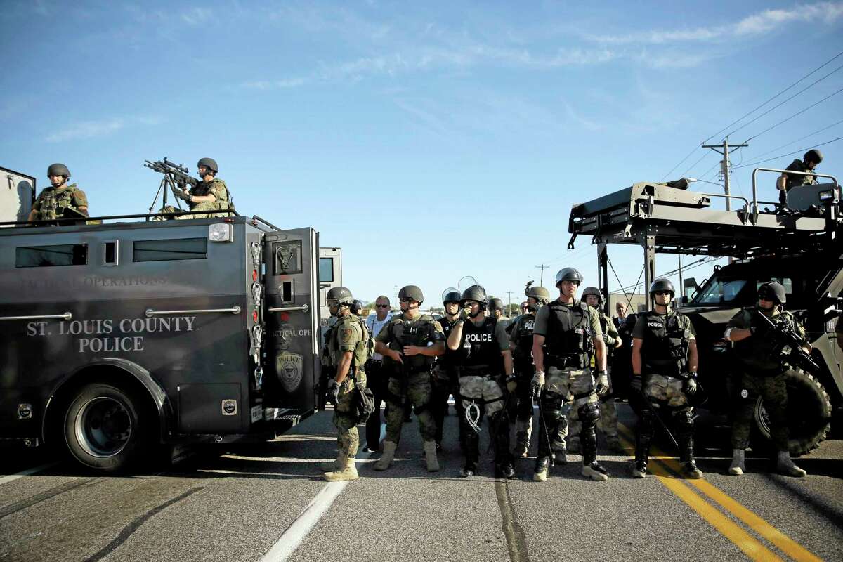 Police in riot gear watch protesters in Ferguson, Mo. on Wednesday, Aug. 13, 2014. On Saturday, Aug. 9, 2014, a white police officer fatally shot Michael Brown, an unarmed black teenager, in the St. Louis suburb. (AP Photo/Jeff Roberson)