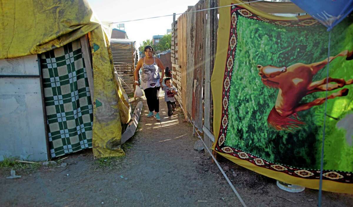 A woman and a child walk between rows of shacks in a squatters camp in Buenos Aires, Argentina, Thursday, March 13, 2014. Squatters that occupied land in demand for housing solutions some weeks ago, name the settlement, "Pope Francis neighborhood" in honor of the Argentine Pope. (AP Photo/Natacha Pisarenko)