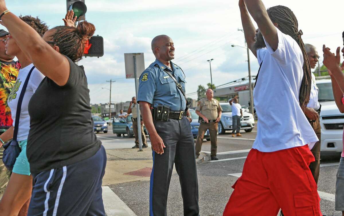 Capt. Ronald Johnson of the Missouri Highway Patrol smiles at demonstrators marching along West Florissant Avenue in Ferguson, Mo., on Thursday, Aug. 14, 2014. The Missouri Highway Patrol seized control of a St. Louis suburb Thursday, stripping local police of their law-enforcement authority after four days of clashes between officers in riot gear and furious crowds protesting the death of an unarmed black teen shot by an officer. (AP Photo/St. Louis Post-Dispatch, David Carson)
