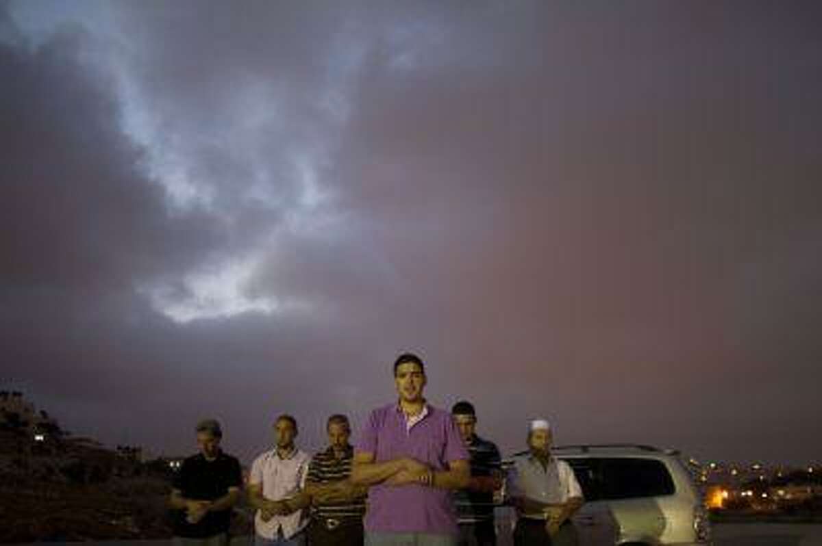 Palestinian men from the Israeli occupied West Bank pray as they wait close to the Israeli military prison of Ofer, in the village of Betunia, for the release of Palestinian prisoners on August 13, 2013.