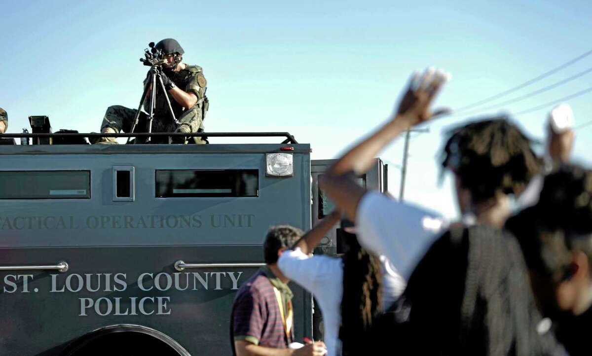 A member of the St. Louis County Police Department points his weapon in the direction of a group of protesters in Ferguson, Mo. on Wednesday, Aug. 13, 2014. On Saturday, Aug. 9, 2014, a white police officer fatally shot Michael Brown, an unarmed black teenager, in the St. Louis suburb.