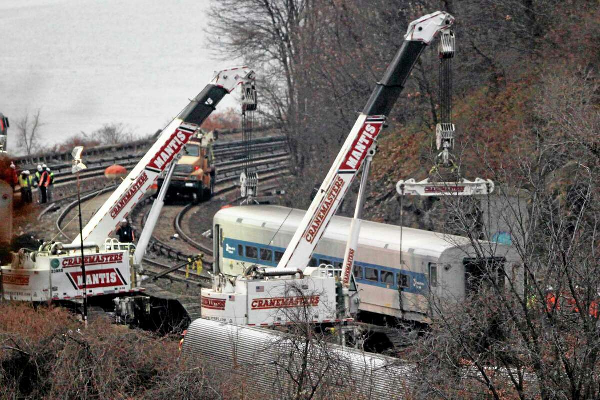 Cranes lift a derailed Metro-North train car, Monday, Dec. 2, 2013, in the Bronx borough of New York. Federal authorities began righting the cars Monday morning as they started an exhaustive investigation into what caused a New York City commuter train rounding a riverside curve to derail, killing four people and injuring more than 60 others. A second "event recorder" retrieved from the train may provide information on the speed of the train, how the brakes were applied, and the throttle setting, a member of the National Transportation Safety Board said Monday. (AP Photo/Mark Lennihan)