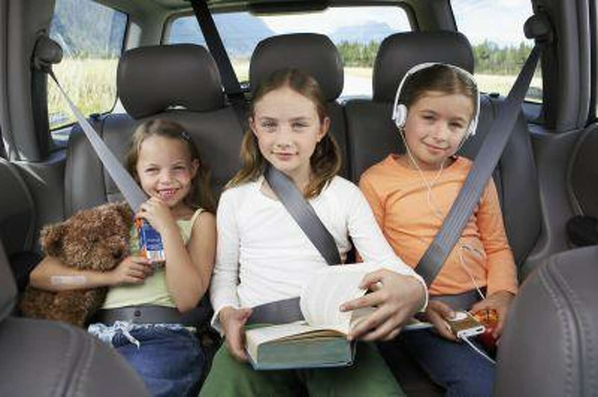 Three girls (6-8 years) sitting on rear seat of car, smiling, portrait