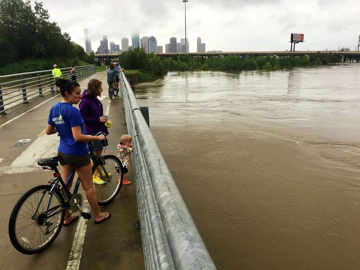People take advantage of a lull in the rains from Tropical Storm Harvey to check out White Oak Bayou from a bike path in the Heights.