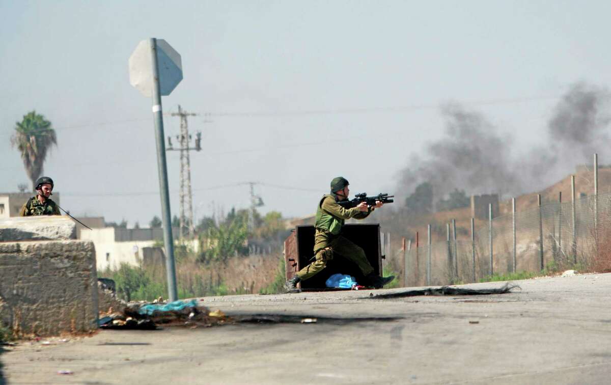 An Israeli soldier fires towards Palestinian protesters, following a protest against the war in the Gaza Strip, during clashes near the West Bank town of Tulkarem on Friday, Aug. 1, 2014. A Palestinian man was shot and later died during clashes with Israeli troops near Tulkarem, Palestinian security sources said. (AP Photo/Mohammed Ballas)