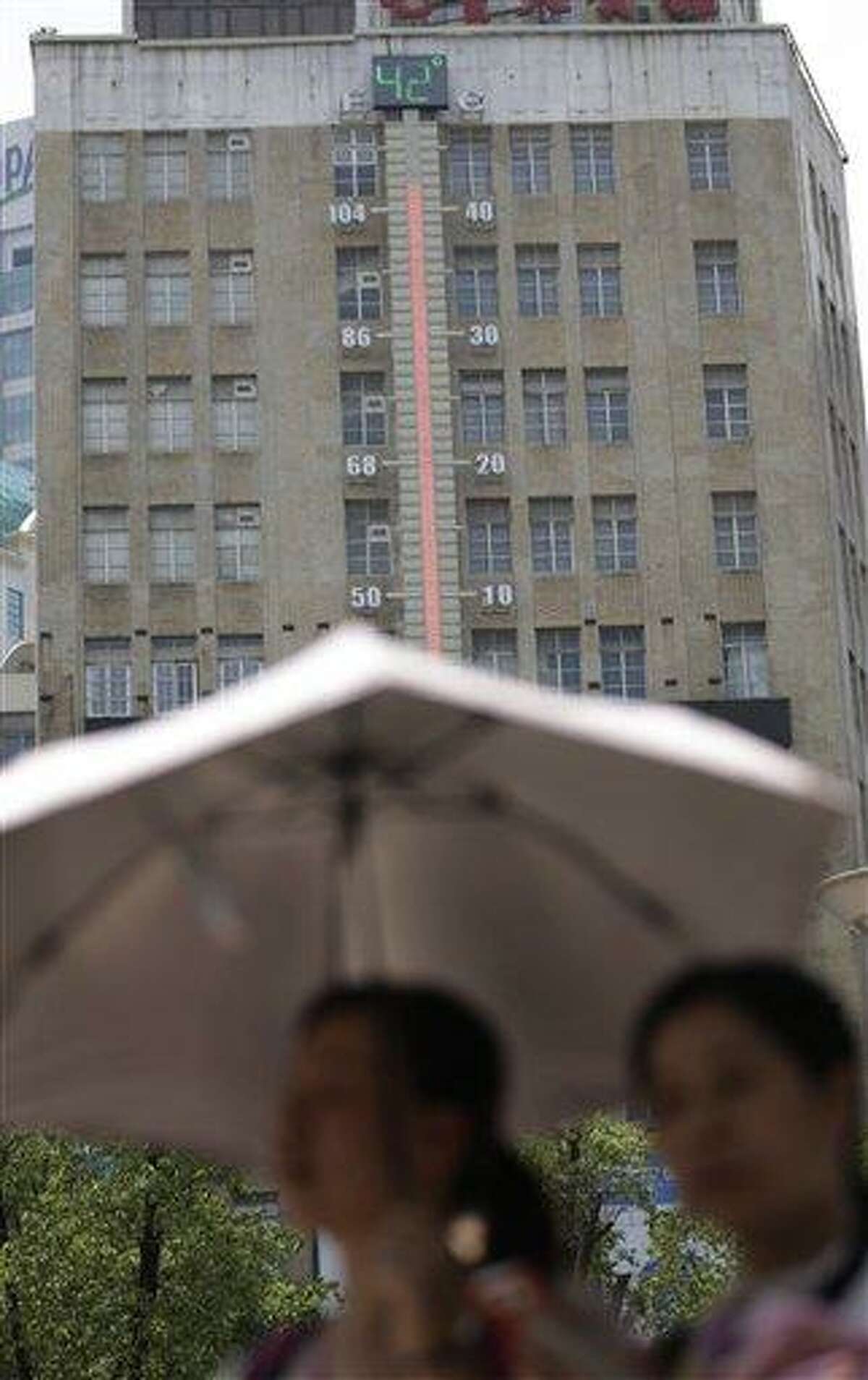 Women walk near a giant thermometer on the building which indicates the current highest temperature in Shanghai, China, Thursday, Aug. 1, 2013. Hot weather has set in with temperatures rising up to 40 degrees Celsius (104 degrees Fahrenheit) in Shanghai. (AP Photo/Eugene Hoshiko)