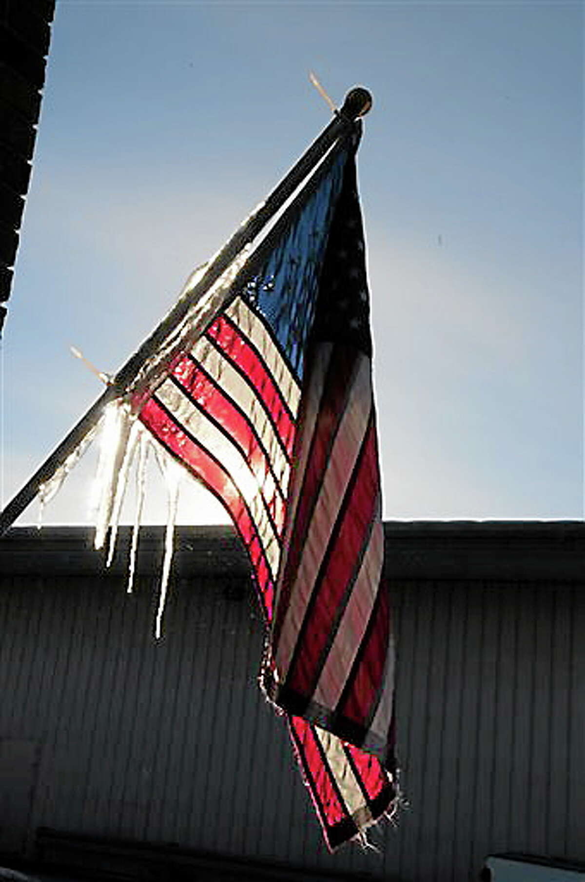 Icicles form on a U.S. flag located under melting snow on the roof of a store in Baxter, Minn. on Wednesday, Dec. 26, 2012. Cold temperatures are beginning to ease in Central Minnesota after a Christmas holiday with temperatures dipping below zero. (AP Photo/Brainerd Dispatch, Steve Kohls)