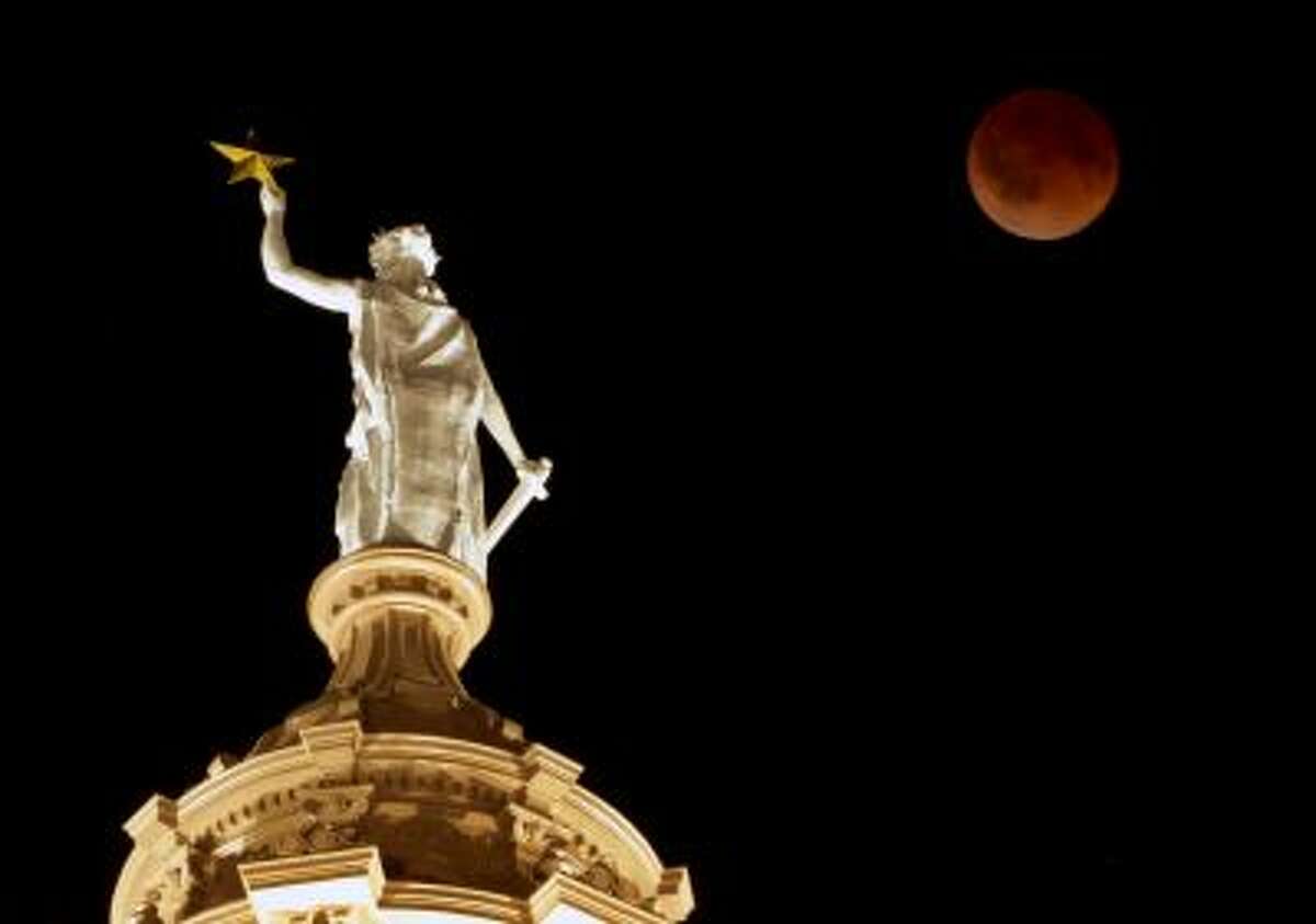 The moon glows a red hue over the Goddess of Liberty statue atop the Capitol in Austin, Texas, during a total lunar eclipse Tuesday, April 15, 2014. Tuesday's eclipse is the first of four total lunar eclipses that will take place between 2014 to 2015. (AP Photo/Austin American-Statesman, Jay Janner) AUSTIN CHRONICLE OUT, COMMUNITY IMPACT OUT, INTERNET AND TV MUST CREDIT PHOTOGRAPHER AND STATESMAN.COM, MAGS OUT