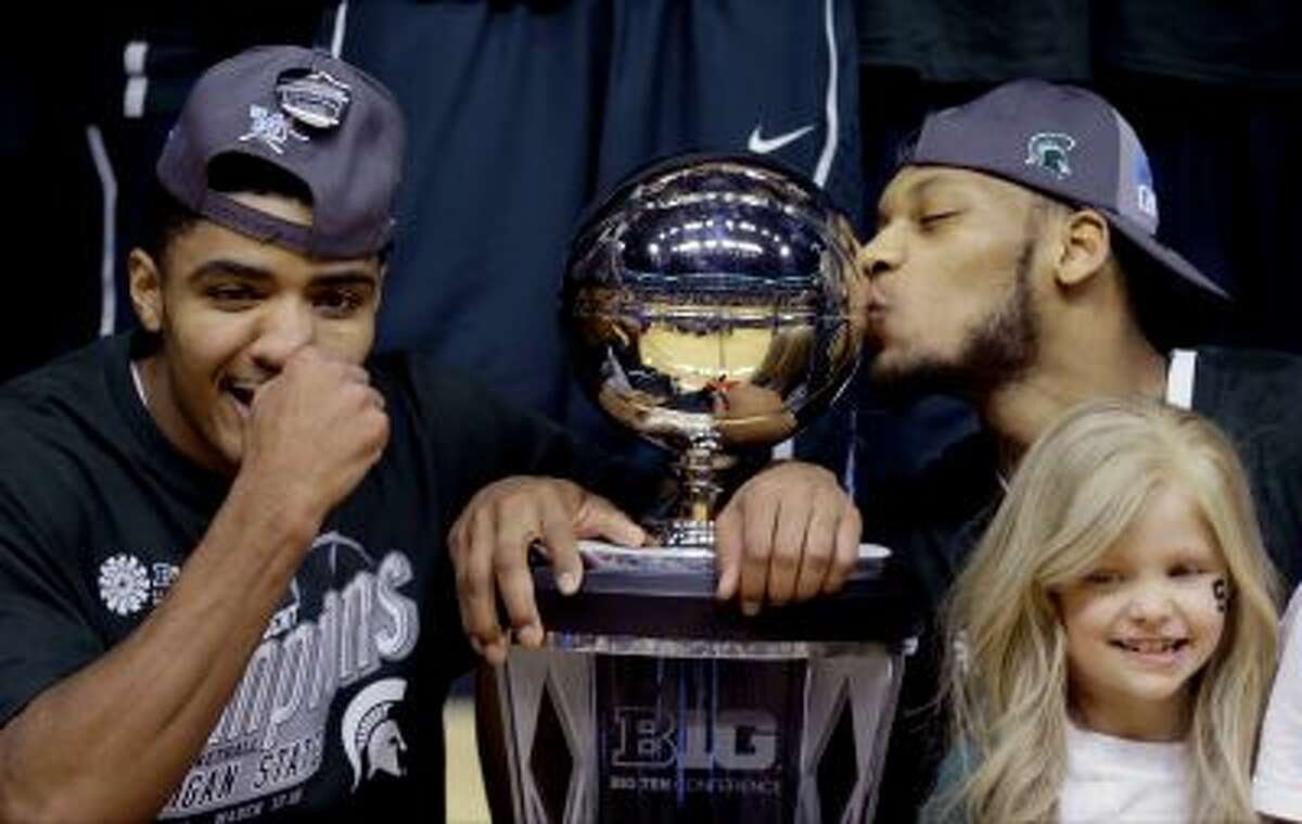 FILE - In this March 16, 2014 file photo, Michigan State's Gary Harris, left, poses with the championship trophy as Adreian Payne kisses it after they defeated Michigan 69-55 in an NCAA college basketball game in the championship of the Big Ten Conference tournament in Indianapolis. Lacey Holsworth, who is batling cancer, smiles at right foreground. The father of 8-year-old Lacey Holsworth, who befriended Michigan State basketball star Adreian Payne says his daughter has died. Matt Holsworth says Lacey Holsworth died at their St. Johns, Mich., home late Tuesday, April 8, 2014, "with her mommy and daddy holding her in their arms."(AP Photo/Michael Conroy)