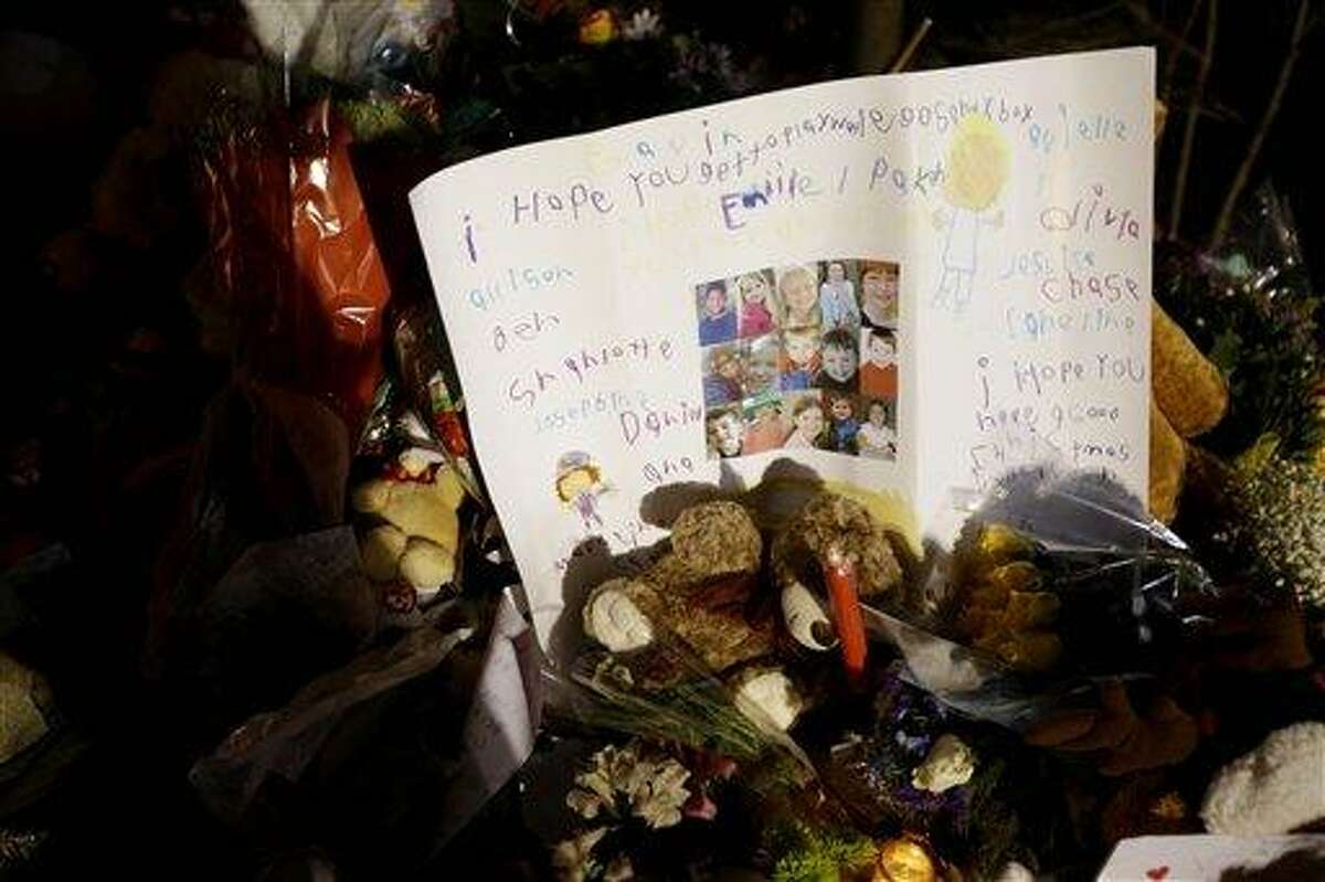 A poster written by children with the faces of some of the victims is among the many tributes at a memorial to the shooting victims in the Sandy Hook village of Newtown, Conn., Thursday, Dec. 20, 2012. Adam Lanza walked into Sandy Hook Elementary School in Newtown, Dec. 14, and opened fire, killing 26 people, including 20 children, before killing himself.(AP Photo/Seth Wenig)