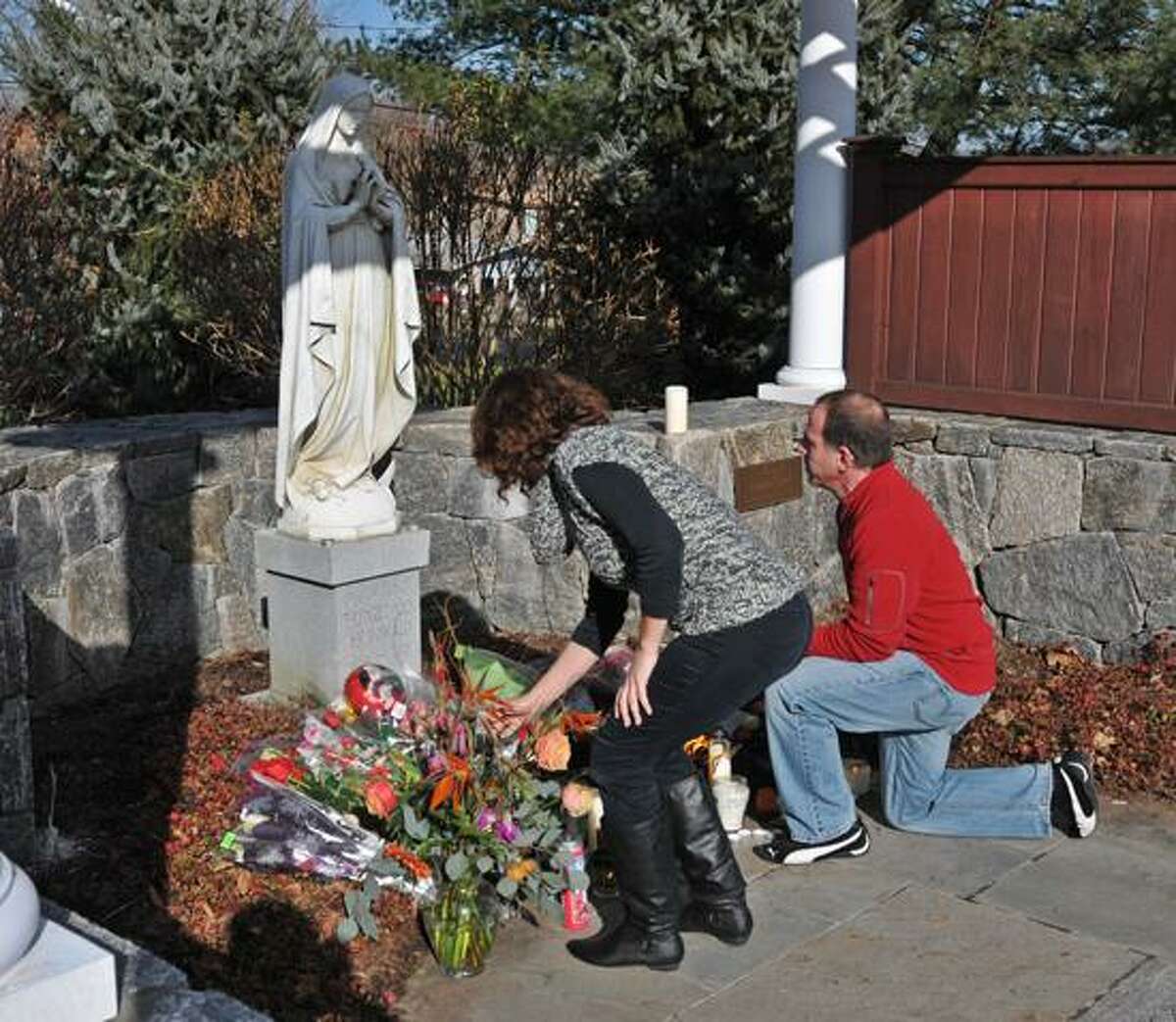 Randy and Paul Convertito of Brookfield place flowers at a statue outside the St. Rose of Lima Church in Newtown. Peter Casolino/New Haven Register