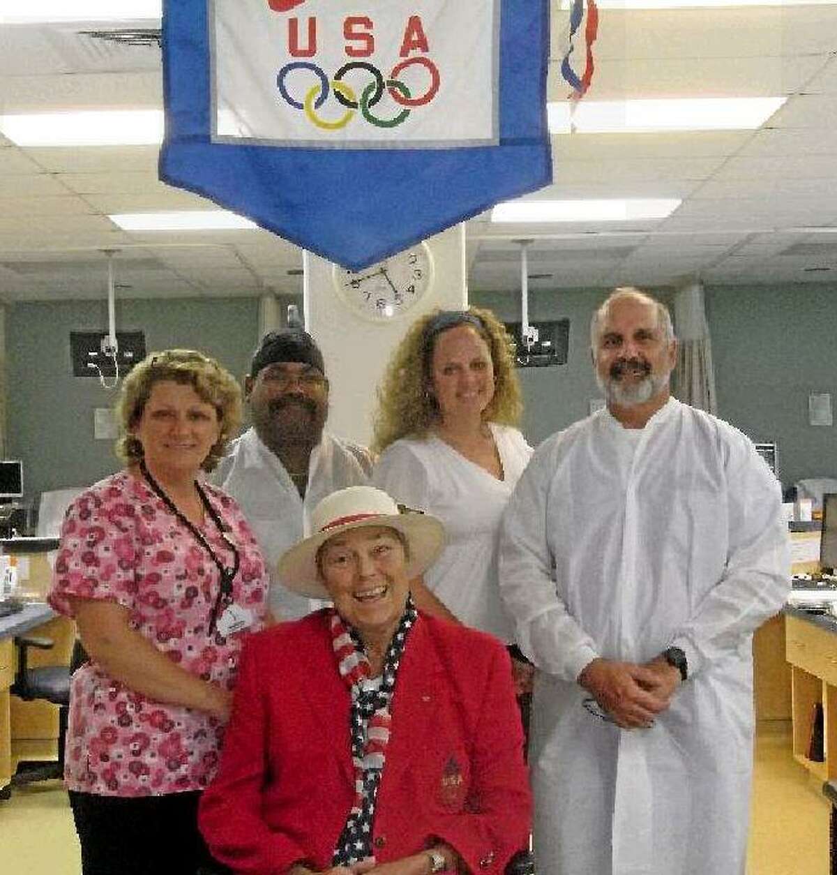 Darlene "Poochie" Montgomery (front) was selected to be one of the first women to demonstrate judo in the 1980 Olympics, which the United States boycotted. Now, she has a new Olympic team at DaVita Dialysis in Torrington, standing under her Olympic flag signed by the 1980 Olympic judo team. Montgomery is wearing the American Olympic outfit from the 1996 games during which she was the manager of the United States' judo team. Back, from left to right: Jo Madia, Nelson Vega, Tracy Morales-Gabelman and Alex Gubbiotti. (MICHELLE MERLIN/Register Citizen)