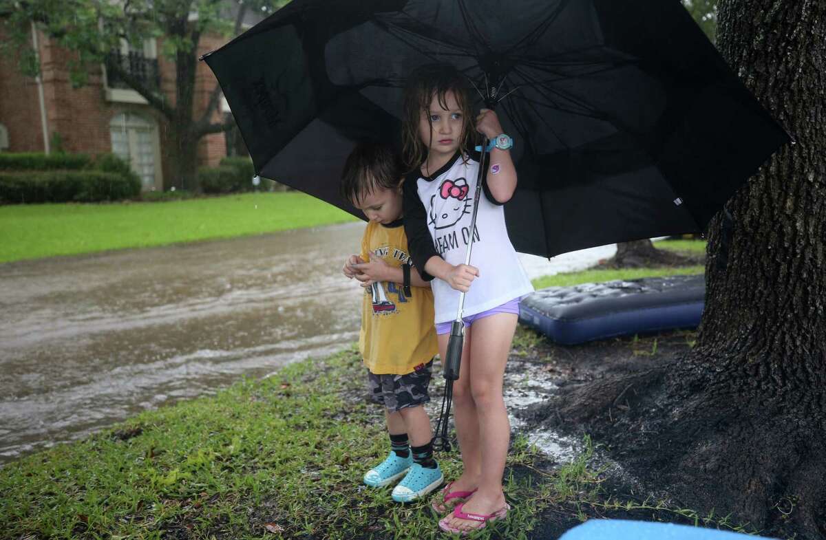Two children use an umbrella while staying off flooded streets as people were evacuated from their homes near Crossroads and Walkwood drives during Tropical Storm Harvey Monday, Aug. 28, 2017, in Houston.