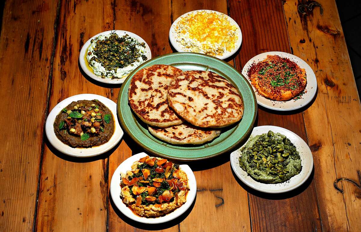 Flatbread is surrounded by sprouted white bean dip with broccoli and chili oil (clockwise from bottom);  preserved eggplant dip with nasturtium capers; spiced yogurt dip with walnuts and dill; bottarga dip with potato and egg; liptauer paprika cheese dip; and pumpkin seed dip with green chili at Duna.