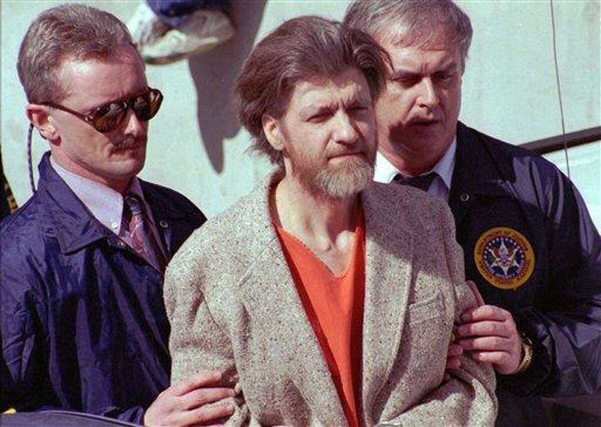 FILE - In this April 4, 1996 file photo, Unabomber Theodore John Kaczynski is flanked by federal agents as he is led to a car from the federal courthouse in Helena, Mont. The 1.4-acre parcel of land in western Montana that was once owned by Kaczynski is on the market for $69,500. The listing offers potential buyers a chance to own a piece of "infamous U.S. history" and says the forested land "is obviously very secluded. (AP Photo/John Youngbear, File)