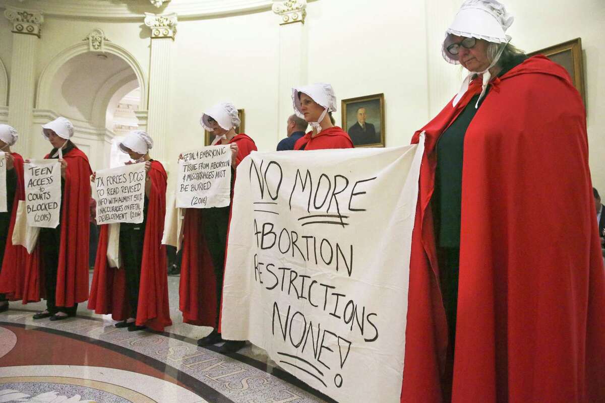 Women dressed in clothing from The Handmaid's Tale stand in silence as abortion rights protestors gather in the Capitol rotunda to protest legislation restricting abortion procedures which eventually passed. A judge in Austin heard testimony in a hearing Tuesday morning seeking to stop a law prohibiting a common second-trimester abortion procedure from taking effect Sept. 1.
