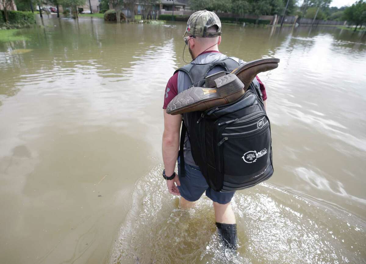 Danny Hannon carries his dry cowboy boots in his backpack as he goes to check his home in the Lakewood Crossing subdivision off Cypresswood Wednesday, August 30, 2017 in Houston. He had almost two feet of water the night before inside his home. Much of the Houston area was flooded in the aftermath of Hurricane Harvey.