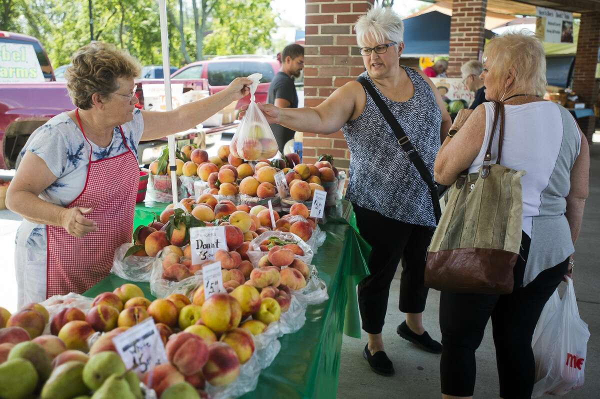 Stormi Sutherland of Midland, center, purchases blackberries from Judy Linton of Midland, an employee of Christofferson Farms of Ludington, on Wednesday, August 30, 2017 at the Midland Farmers Market.
