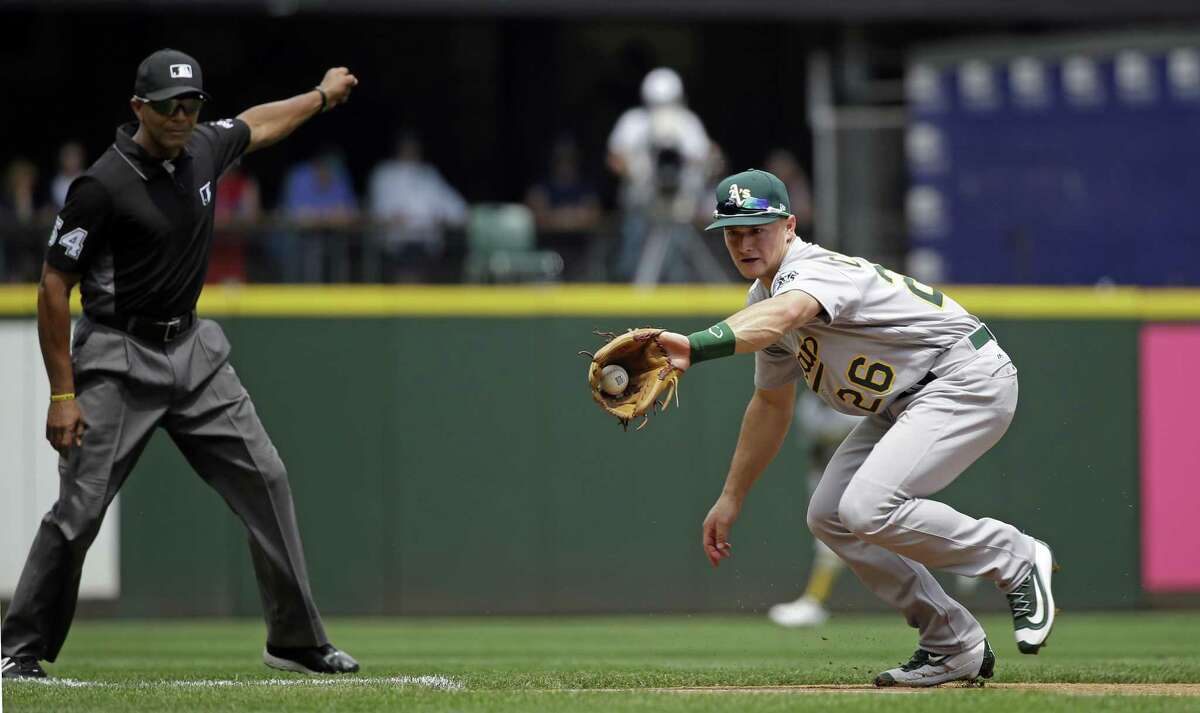 Oakland Athletics third baseman Matt Chapman reaches to snag a grounder down the line from Seattle Mariners' Nelson Cruz as umpire C.B. Bucknor signals a fair ball in the second inning of a baseball game, Sunday, July 9, 2017, in Seattle. Chapman completed the throw to first for the out. (AP Photo/Elaine Thompson)