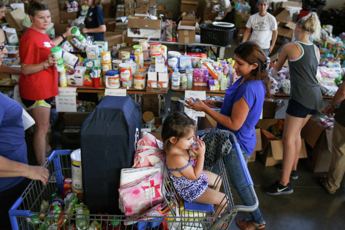 Walden resident Anna Chavarria, right, gathers donated supplies as her daughter Alexandra Zamora, 2, stares off into the distance on Saturday, Sept. 2, 2017, at the Falcon Steel warehouse in Conroe. Hundreds of volunteers flocked to the donated warehouse, which is operating as a donations distribution center for Montgomery County, to help with organization, unloading, distribution and more.